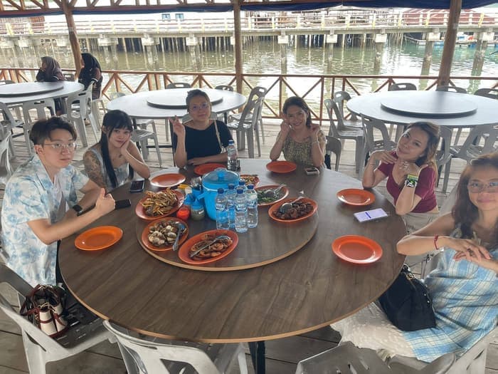 The group around a round table at a seafood restaurant built over the water, with crab, clams and prawns served.