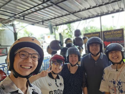 Lai Lai Shun's group in helmets, smiling before an activity, with racks of helmets behind them.