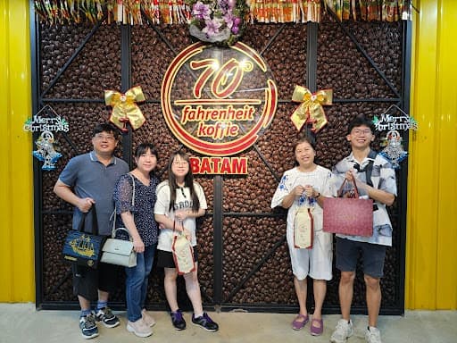 Five travellers at the 70 Fahrenheit Koffie Batam photo wall, decorated with coffee beans and ribbons.