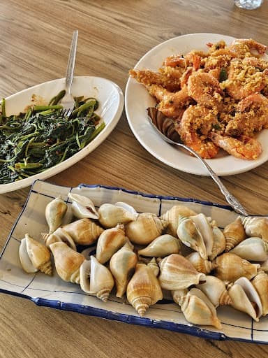 The seafood lunch on a wooden table: stir fried greens, salted egg prawns and a platter of sea snails.
