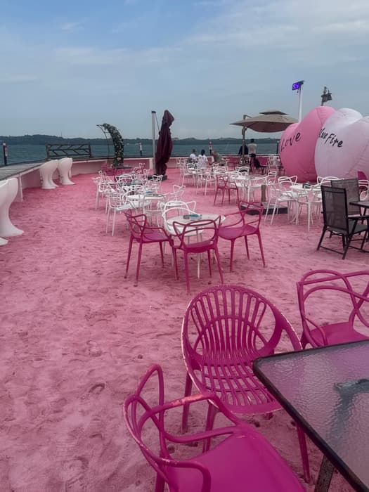 Pink sand and pink chairs set out by the water at a beach club.