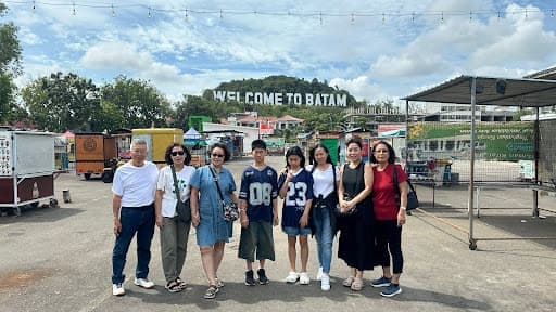 Eight travellers posing together under the Welcome to Batam sign.