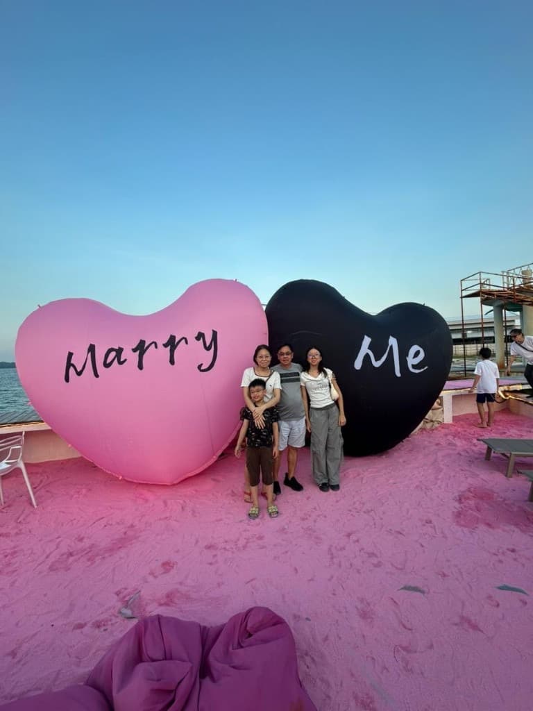 A family between two giant heart sculptures on pink sand at dusk